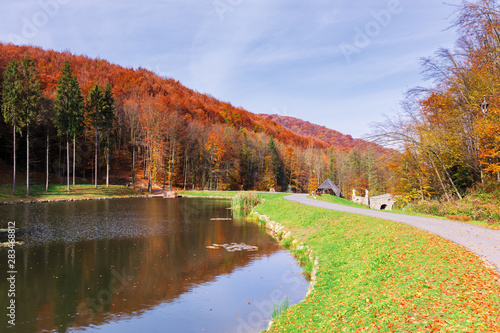 beautiful park in the mountains. wonderful sunny autumn weather. walking path around the pond. trees in fall foliage.  blue sky with clouds