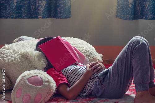 Child tired of reading sleeping on the bed with a book on her face.