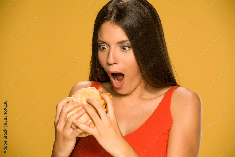 Young greedy woman eating a burger on yellow background Young greedy woman eating a burger on yellow background