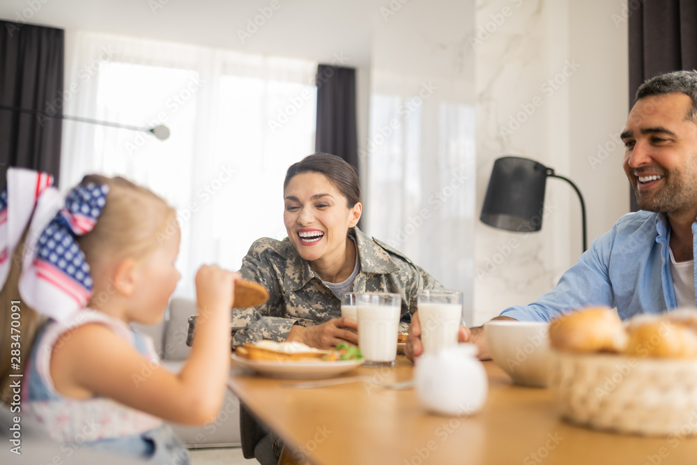 Military woman laughing while looking at her daughter eating cookie Military woman laughing while looking at her daughter eating cookie