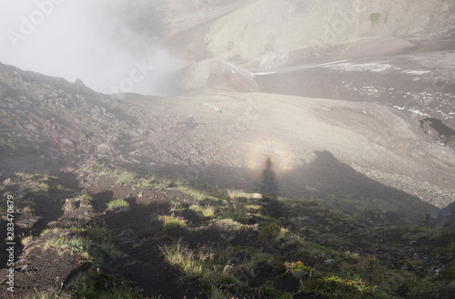 Solar glory and Spectre of the Brocken in misty magical morning in Avacha base camp. Kamchatka Peninsula, Russian far east.  Weather and clouds creating mystical veil of fog in volcanic landscape.