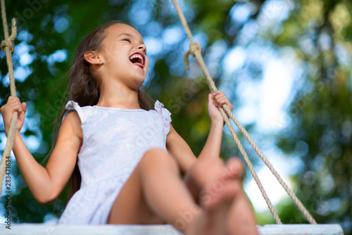 Happy girl rides on a swing in park. Little Princess has fun outdoor, summer nature outdoor. Childhood, child lifestyle, enjoyment, happiness. photo