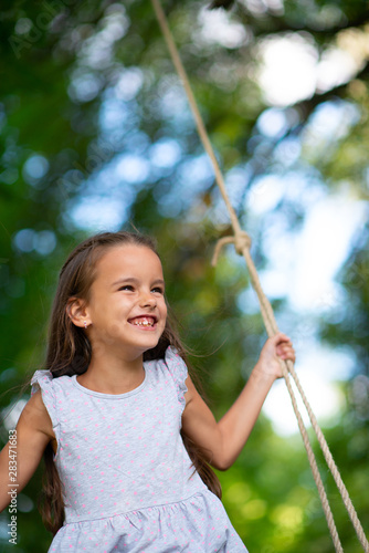 Happy girl rides on a swing in park. Little Princess has fun outdoor, summer nature outdoor. Childhood, child lifestyle, enjoyment, happiness.