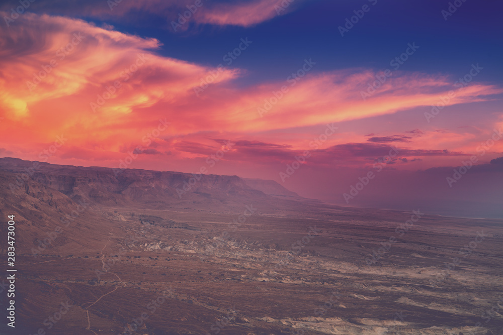 Mountain desert landscape. View of the valley from the mount. Desert in the early morning. Beautiful sunrise over Masada with dramatic sky. The Judaean Desert. Landscape in Dead sea region
