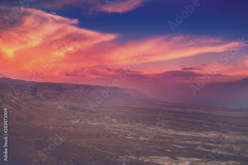 Mountain desert landscape. View of the valley from the mount. Desert in the early morning. Beautiful sunrise over Masada with dramatic sky. The Judaean Desert. Landscape in Dead sea region