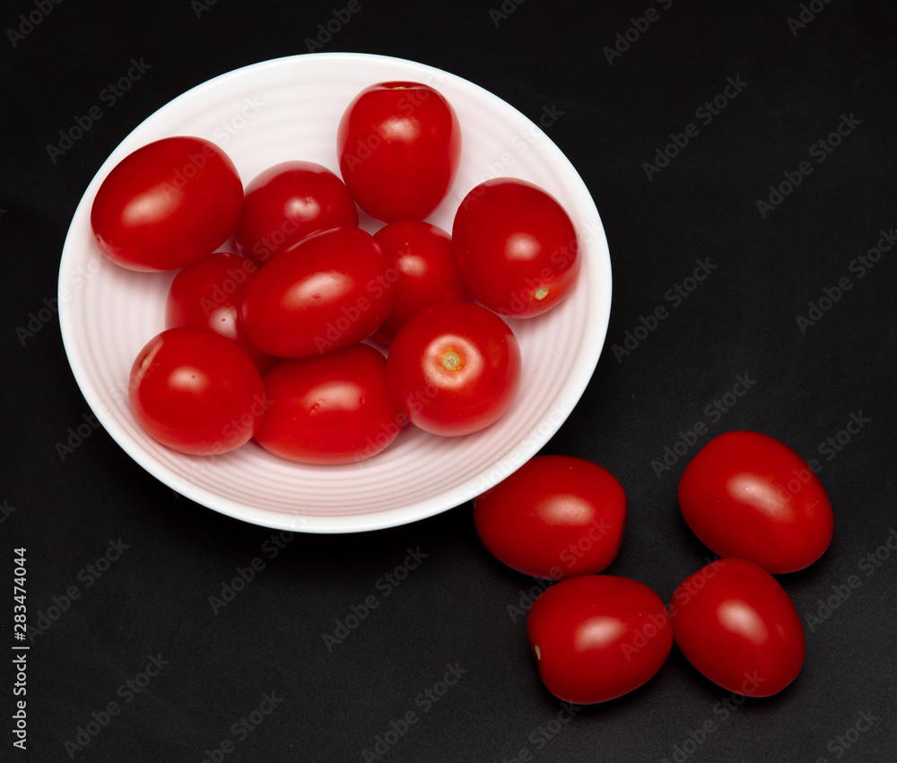 Red cherry tomatoes in a white plate on a black background Red cherry tomatoes in a white plate on a black background