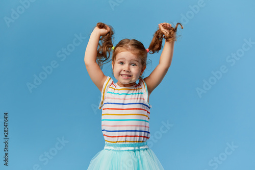 Portrait of surprised smiling cute little toddler girl. child standing isolated over blue background. Looking at camera and laughs
