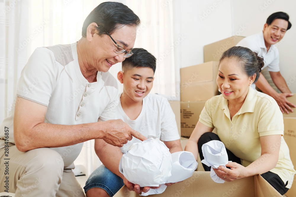 Cheerful grandparents explaining boy how to wrap fragile things before packing the in cardboard boxes Cheerful grandparents explaining boy how to wrap fragile things before packing the in cardboard boxes