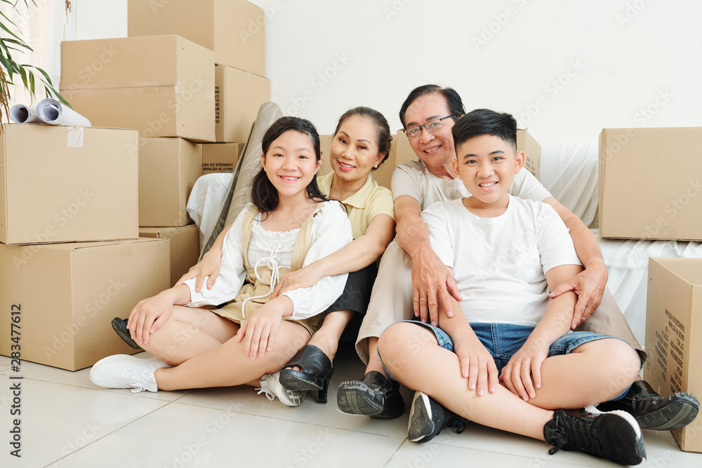 Happy children and grandparents sitting on the floor in living room of new house with many cardboard boxes around Happy children and grandparents sitting on the floor in living room of new house with many cardboard boxes around