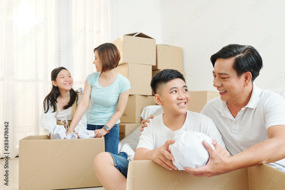 Father helping son to unpack belongings when mother and daughter unwrapping tableware in new house Father helping son to unpack belongings when mother and daughter unwrapping tableware in new house
