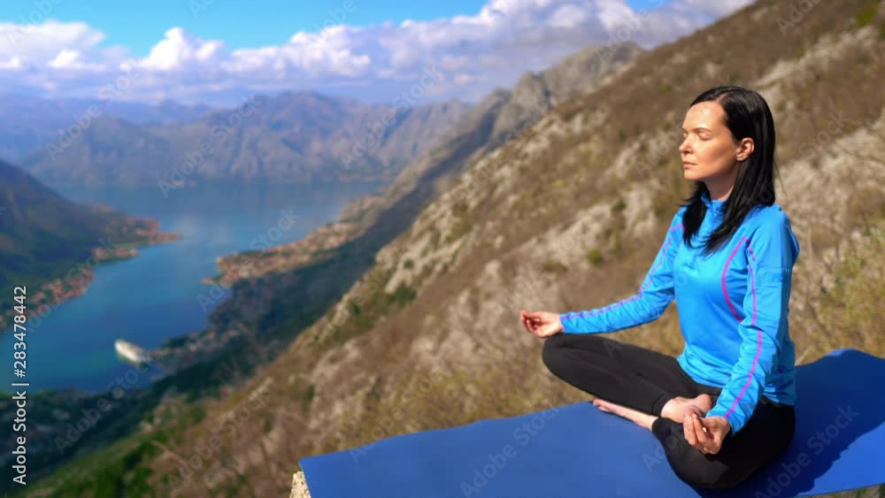 caucasian brunette yogi trains on the top of mountain area amazing view on the skyline with clouds and blue water caucasian brunette yogi trains on the top of mountain area amazing view on the skyline with clouds and blue water