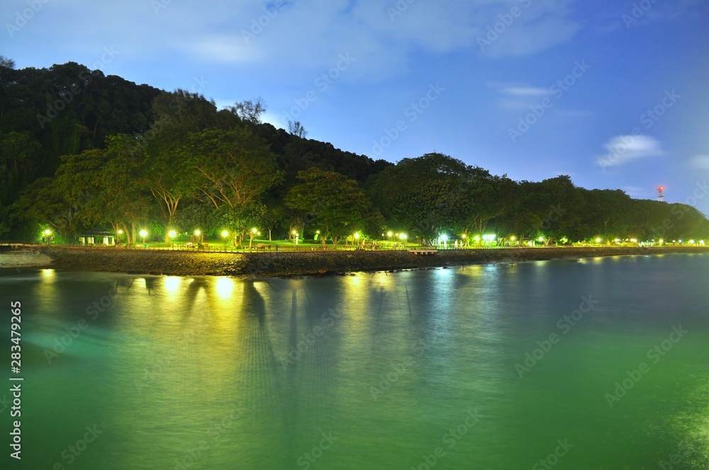 Scenic view of Labrador Park (located in the south of Singapore) with small hill of trees in the background and water in the foreground seen from jetty by night ..