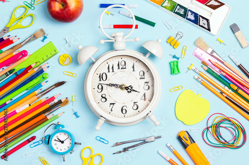 White alarm clock and school supplies on blue background top view.