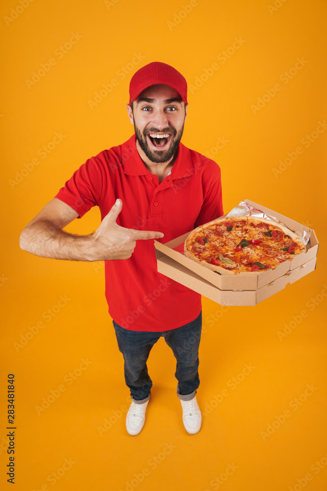 Full length image of attractive delivery man in red uniform smiling and holding pizza box Full length image of attractive delivery man in red uniform smiling and holding pizza box