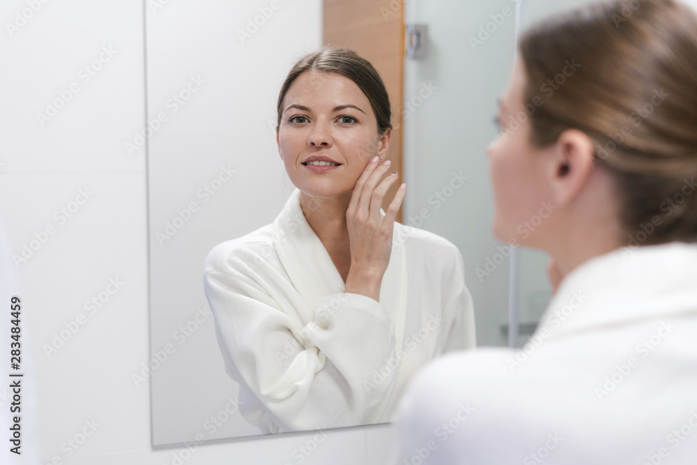Woman in bathrobe looking in mirror at bathroom Woman in bathrobe looking in mirror at bathroom