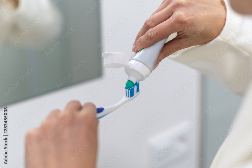Woman in white bathrobe holding toothbrush, standing in bathroom Woman in white bathrobe holding toothbrush, standing in bathroom