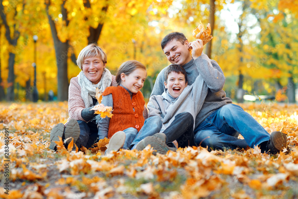 Happy family sitting on fallen leaves, playing and having fun in autumn city park. Children and parents together having a nice day. Bright sunlight and yellow leaves on trees, fall season. Happy family sitting on fallen leaves, playing and having fun in autumn city park. Children and parents together having a nice day. Bright sunlight and yellow leaves on trees, fall season.