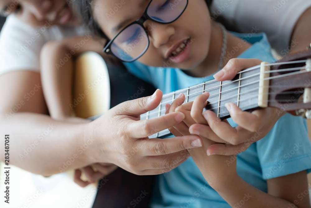 Obraz premium Mother teaching the daughter learning how to play acoustic classic guitar for jazz and easy listening song select focus shallow depth of field