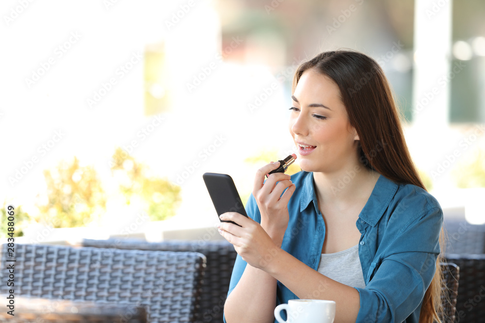 Woman painting lips using a phone as a mirror in a bar Woman painting lips using a phone as a mirror in a bar