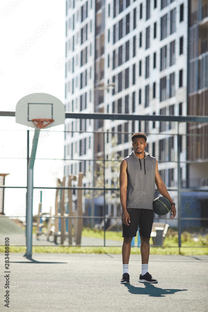 Full length portrait of African basketball player standing by hoop in outdoor court ready to practice, copy space