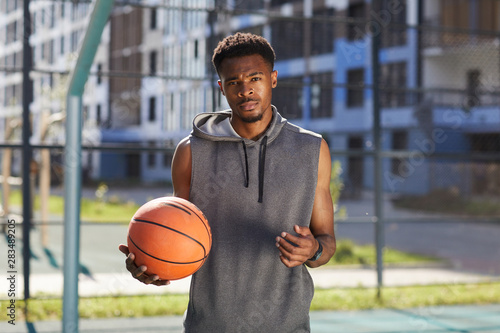 Waist up portrait of African basketball player posing in outdoor court and looking at camera, copy space