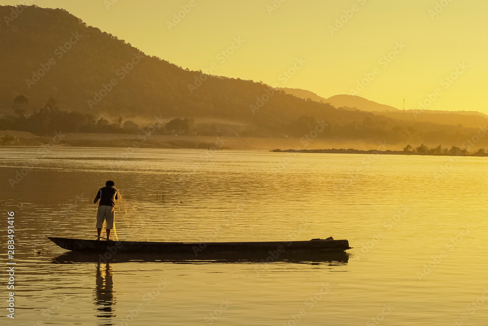 view of a fisherman floating a small boat in Mekong river with yellow sun light background, sunrise at Khong Chiam, Ubon Ratchathani, Thailand.