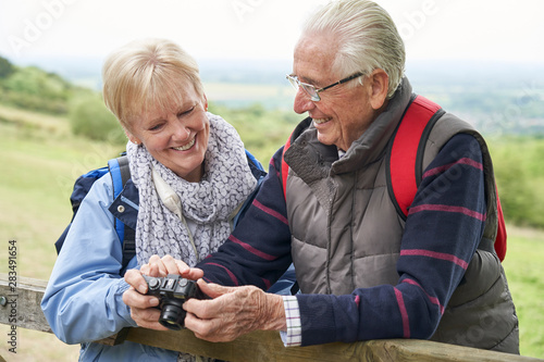 Senior Couple Hiking In Countryside Standing By Gate And Taking Photo With Camera