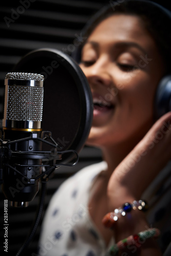 Obraz na plátně Female Vocalist Wearing Headphones Singing Into Microphone In Recording Studio