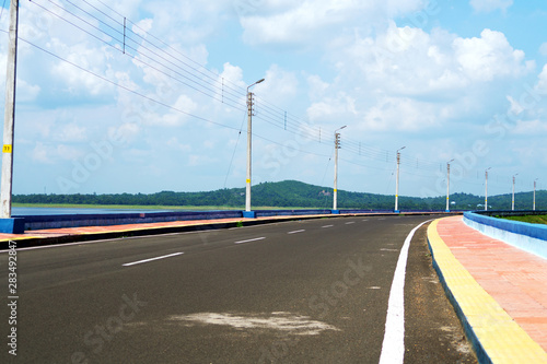 Road with Footpath and electric pillars with street lamp under blue sky