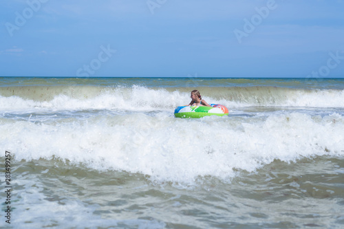 Sea with waves and a girl in an inflatable circle far from the shore. Activities on the beach. © Konstiantyn Zapylaie