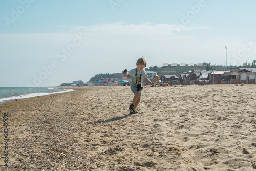A little boy with a camera runs along the seashore.