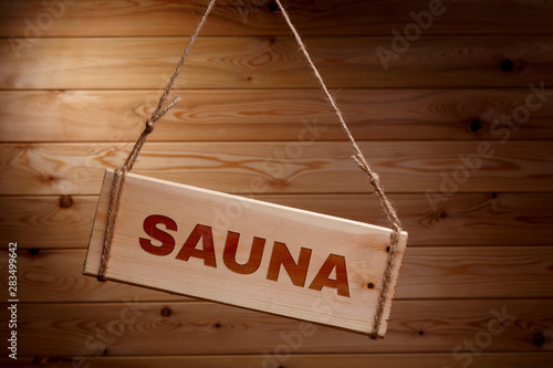 Wooden signboard with the words SAUNA on a rough rope on a beautiful wooden background