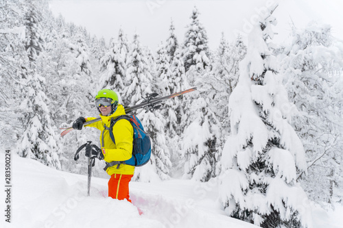 Man in yellow with blue backpack skiing stay with many firs around and soft powdery snow. The backcountry skier is on Alps Mountain in Austria.