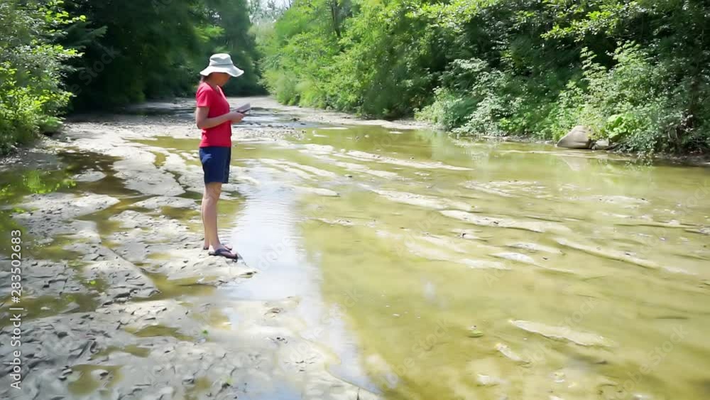 walks in the wild on a sunny summer day.young woman on a walk on the shore of a mountain river.girl takes pictures of the surrounding space on a modern electronic device. walks in the wild on a sunny summer day.young woman on a walk on the shore of a mountain river.girl takes pictures of the surrounding space on a modern electronic device.