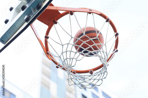 Closeup of basketball shooting through hoop against urban background, copy space © Seventyfour