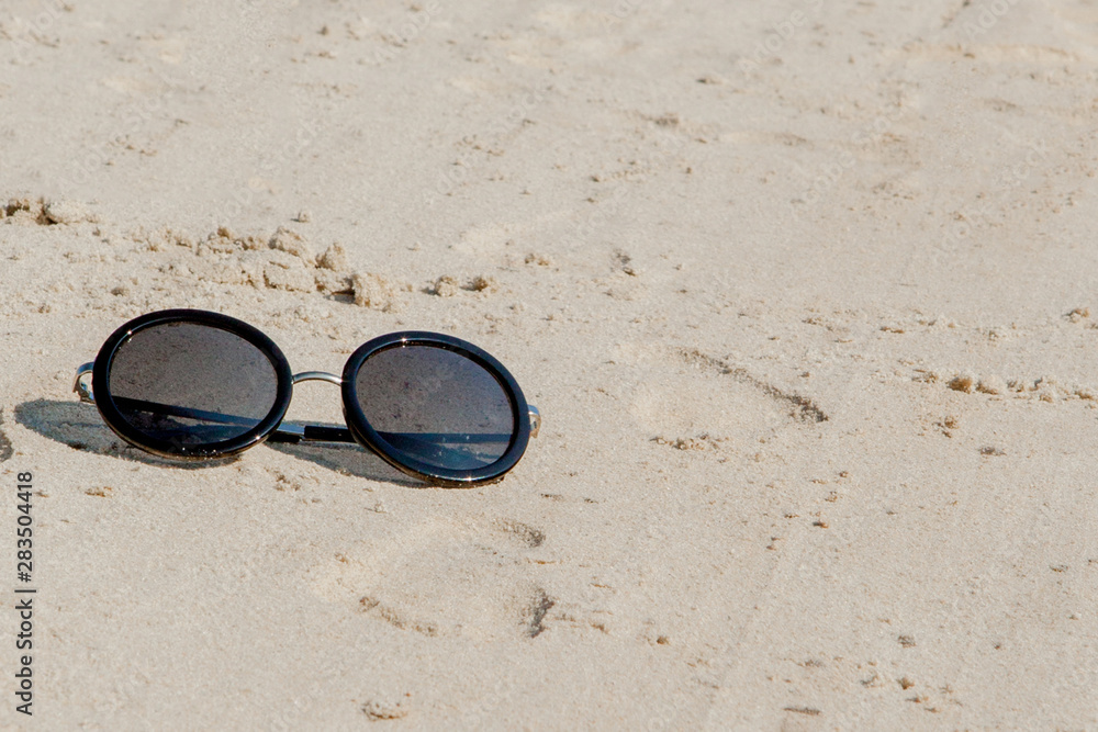 Top view of sunglasses on the beach near the blue sea with sand