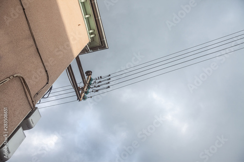 Obsolete old electrical power lines, with their vintage isolators, abiding by former industrial European standards, on a old building in a French village behind a grey sky