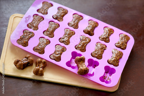Cooking the homemade biscuits for dogs, bone-shaped in silicone mold, taken out of the oven. Dog treats from liver and carrot. Indoors, copy space, close up, selective focus.