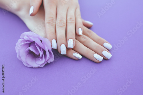 Purple manicure on a plain background with a flower.