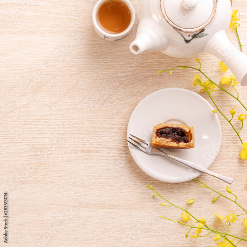 Tasty moon cake for Mid-Autumn festival on bright wooden table, concept of festive afternoon tea decorated with yellow flowers, top view, flat lay. photo