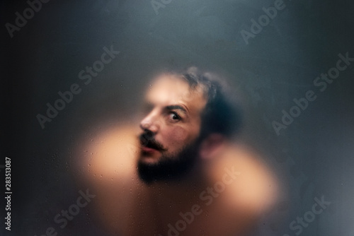 Creepy looking man with one eye behind a frosted glass.