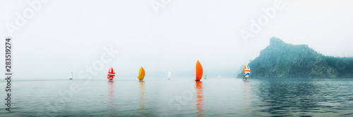 Yacht regatta with an orange sail in a foggy morning floats on the sea