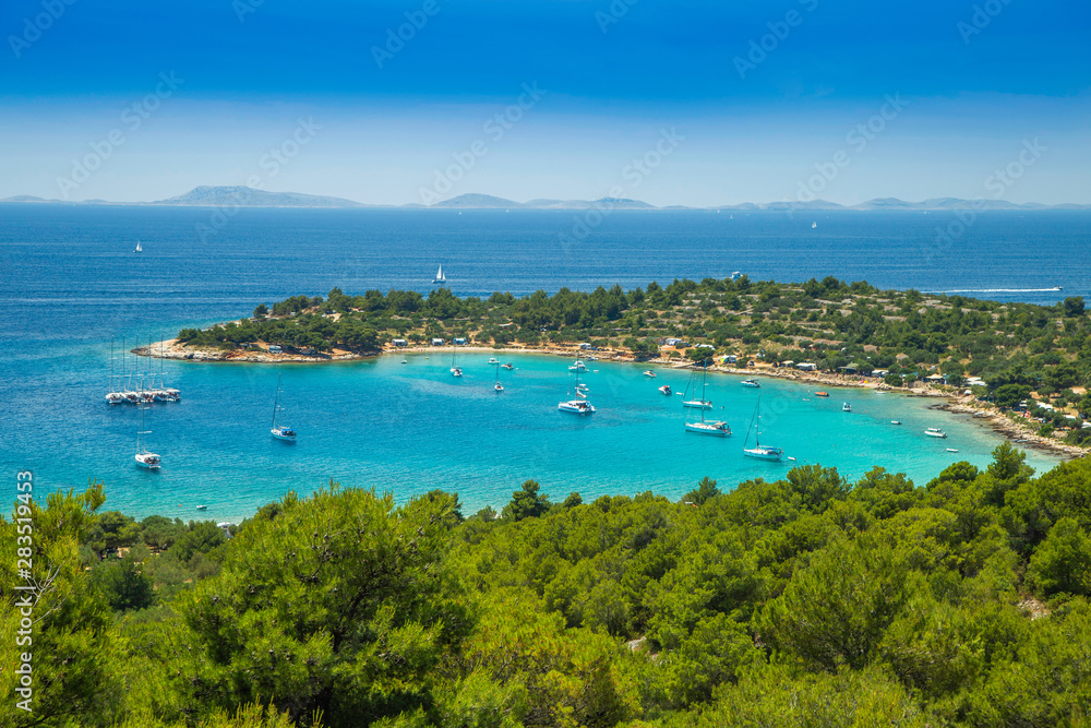 Panoramic view on Kosirina beach lagoon on Murter island in Croatia, anchored sailing boats and yachts on blue sea