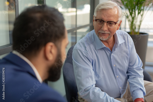 Handsome grey-haired man looking at his colleague