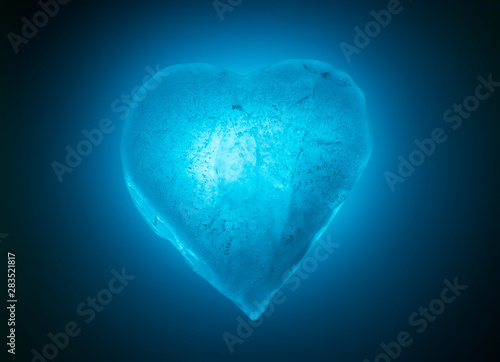 Ice frozen heart symbol of blue color close-up glowing in blue cold light. Texture of ice with bubbles.