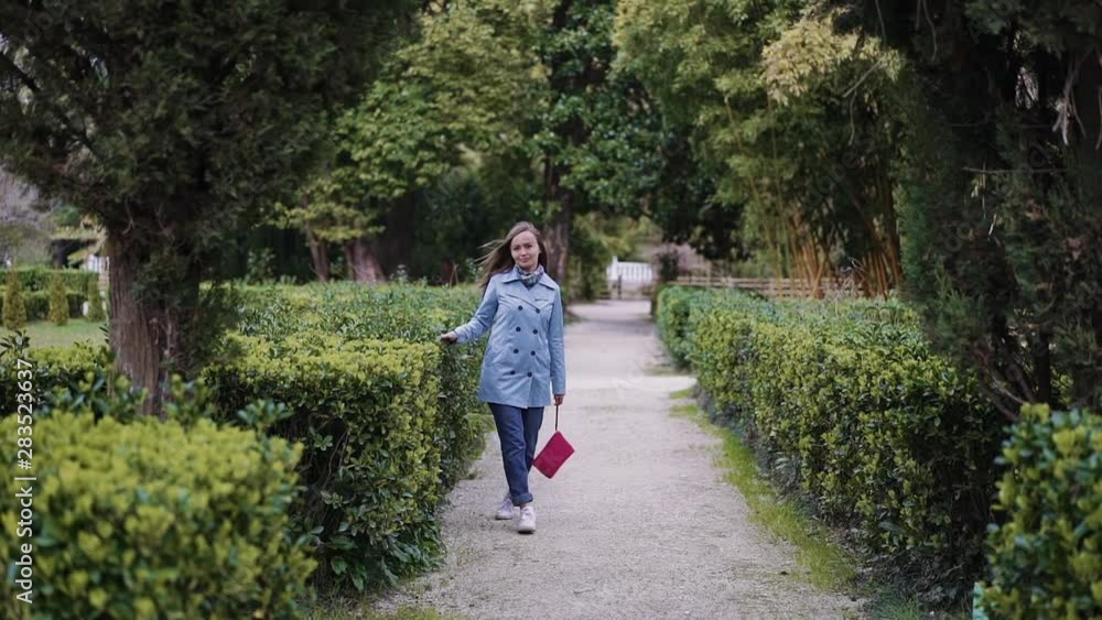 Girl walks in the park along the sheared green bushes and leads her hand over the leaves, general plan Girl walks in the park along the sheared green bushes and leads her hand over the leaves, general plan