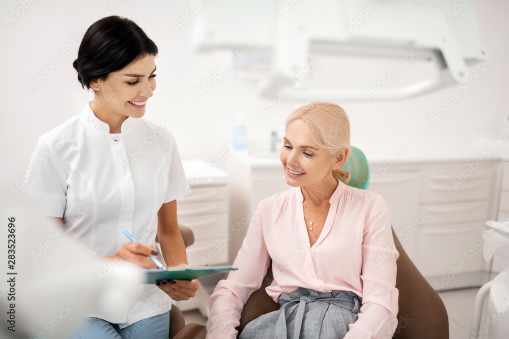 Fototapeta premium Smiling woman sharing her personal information with her dentist.