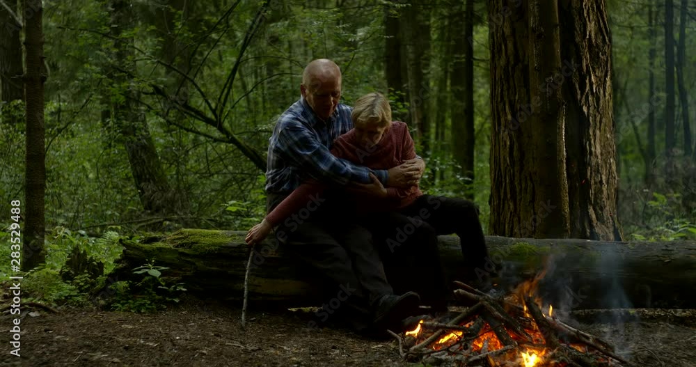 An elderly couple sitting in the woods in the evening on a log and bask. The gentle embrace of people who have lived a long life together An elderly couple sitting in the woods in the evening on a log and bask. The gentle embrace of people who have lived a long life together
