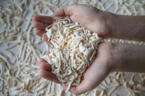 Girl holding handful freshly cooked raw homemade noodles in her hands on noodle or pasta background. Closeup, selective focus