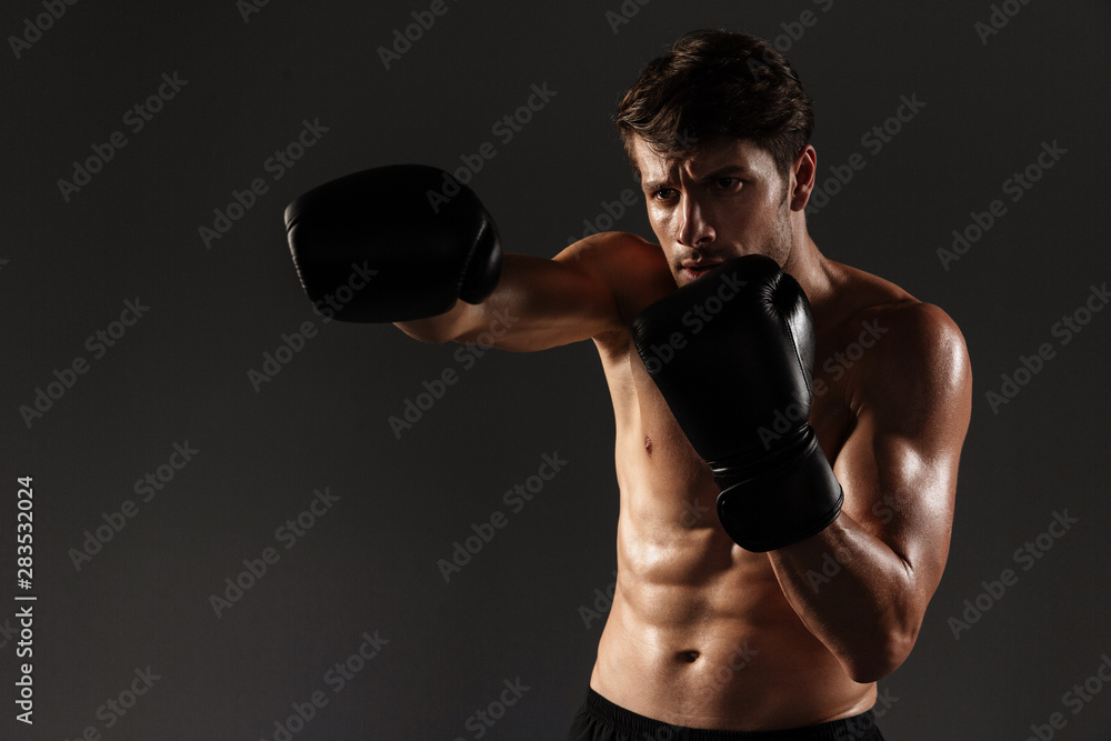 Handsome young strong sportsman boxer in gloves make exercises boxing isolated over black wall background.